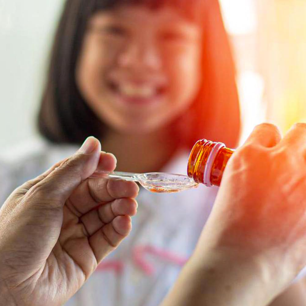 Child smiling while receiving syrup from a bottle, showcasing a caring moment in a family setting.